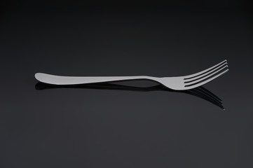Elegant shiny silver fork on black mirror background.