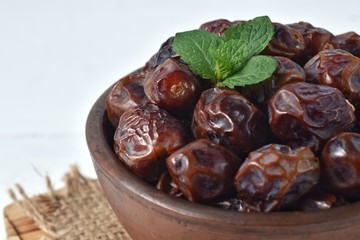 dried date and green mint in a bowl on white wooden table.