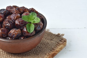dried date and green mint in a bowl on white wooden table.