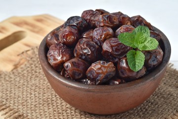 dried date and green mint in a bowl on white wooden table.