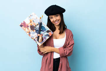 Fototapeta premium Young artist woman holding a palette over isolated blue background laughing.
