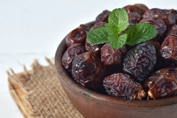 dried date and green mint in a bowl on white wooden table.