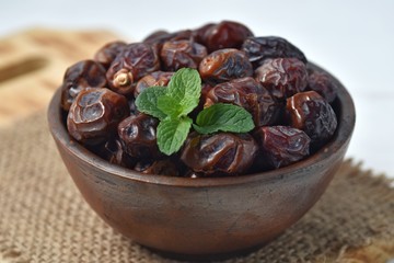 dried date and green mint in a bowl on white wooden table.