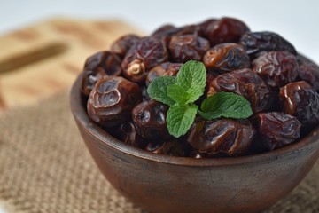 dried date and green mint in a bowl on white wooden table.