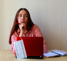 A girl sits dreamily at the table with a computer and a copybooks. The schools, institutes and universities are closed on quarantine due to the pandemic of coronavirus Covid-19. Distance education 