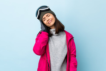 Mixed race skier girl with snowboarding glasses over isolated blue background with headache.