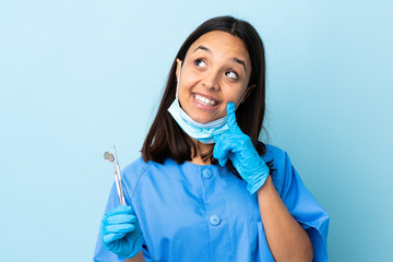 Young brunette mixed race dentist woman holding tools over isolated background thinking an idea while looking up