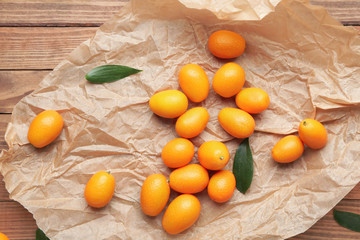Parchment with tasty kumquat fruit on wooden background