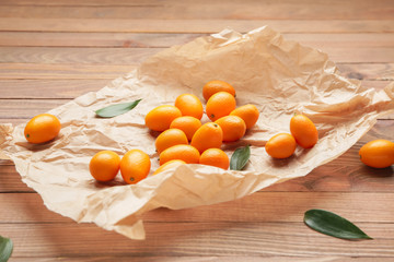 Parchment with tasty kumquat fruit on wooden background