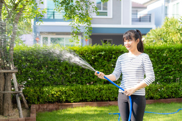 Asian woman having happy in home backyard summer garden, with garden hose splashing water on the...