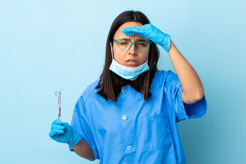 Young brunette mixed race dentist woman holding tools over isolated background looking far away with hand to look something