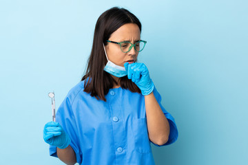 Young brunette mixed race dentist woman holding tools over isolated background coughing a lot