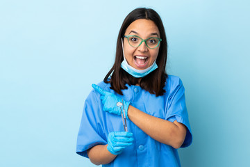 Young brunette mixed race dentist woman holding tools over isolated background surprised and pointing side