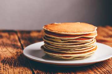 Stack of american pancakes on white plate over wooden table