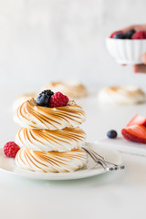 A stack of toasted meringues and berries with a hand holding a small bowl of berries in behind.