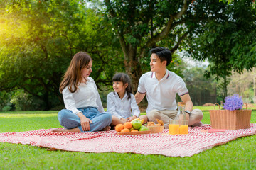 Asian teen family happy holiday picnic moment in the park with mother and daughter looking at father and smile to happy spend vacation time togerter in green garden with friut and food..