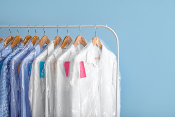 Rack with clothes after dry-cleaning on color background