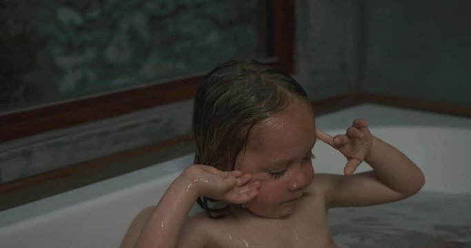 Preschooler in bathtub with his mother rubbing his eyes