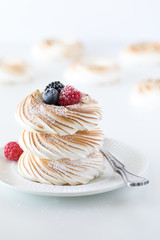 A stack of toasted meringues and berries against a white background with other meringues in soft focus in behind.