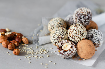 Vegan energy balls with hazelnut on a gray background. Natural sweets from nuts and dried fruits in coconut, cocoa and sesame seeds, close-up. Sugar-free and gluten-free sweets, raw food desserts