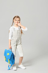 Cute little schoolgirl showing thumb-up on light background