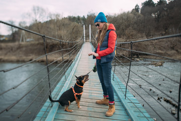 A woman walks with a dog over the river on a suspension bridge. Young girl with a Bull terrier on a...