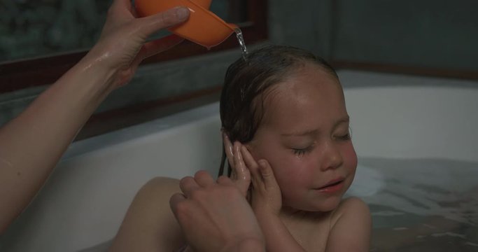 Preschooler having his hair washed in bathtub by mother