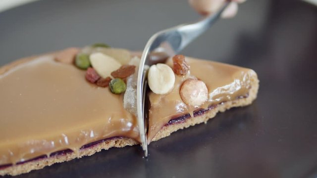 Eating chocolate caramel sweets tart with silver fork. Close up on beautiful tart with nuts and candied fruits.