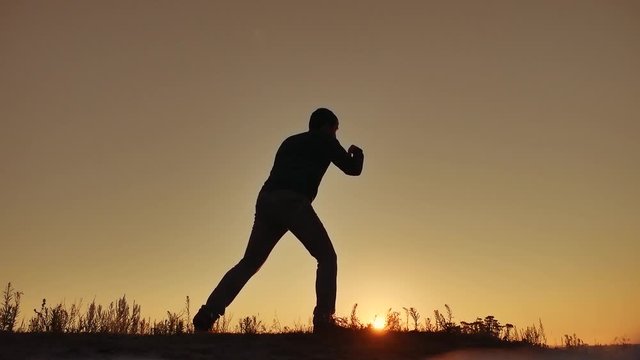 man is training doing an imitation boxing lifestyle shadow fight. martial arts concept. silhouette man on a hill nature sunlight engaged in hand-to-hand combat