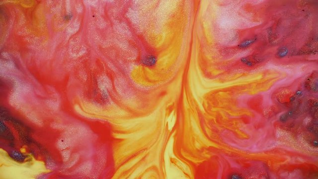 Colorful red and orange paint spreading on universe colors surface mix in fantastic design and patterns. Gold dust sparkling particles, ink drops and mixing. Multicolored background in motion