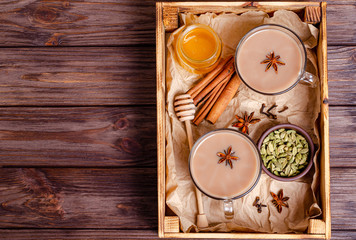 Glass cups of traditional indian chai masala tea on a tray with ingredients.