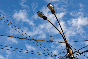 Concrete electric pole with street lights and lots of wires against a blue sky