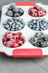 Frozen raspberries, blueberries and blackberries in a white iron baking dish on a gray concrete background.