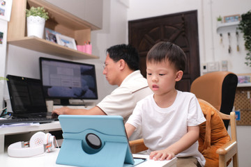 Stay Home Stay Safe, Father and son using computers at home, Coronavirus pandemic prevention, Businessman working from home, kindergarten closed, while in quarantine during the Covid-19 health crisis
