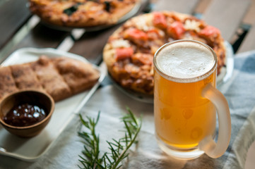 Fresh beer in the glass with Homemade pizza on the background closeup. Selective focus with light from the window