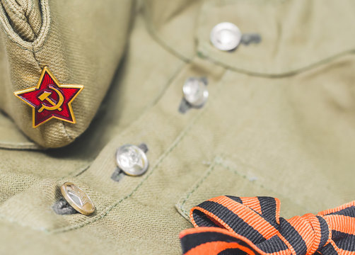 9 May Victory day 1945 holiday background. Closeup of forage cap with Red Army star and St. George ribbon lying on Soviet army military tunic uniform. Top view, layout, copy space.