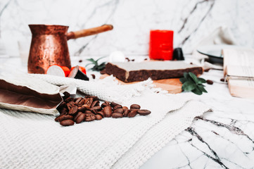 scattered fried coffee beans on white marble and Metal Turkish coffee pot with a long wooden handle and scented candles on the background. Beautiful self-isolation