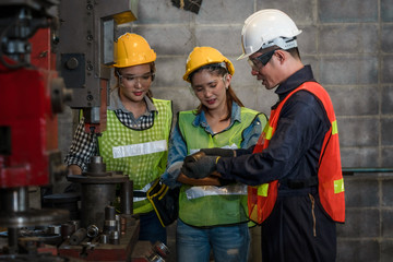 industrial background of asian male mechanic engineer supervisor explaining machine work procedure to new female mechanic engineer in metal work manufacturing factory