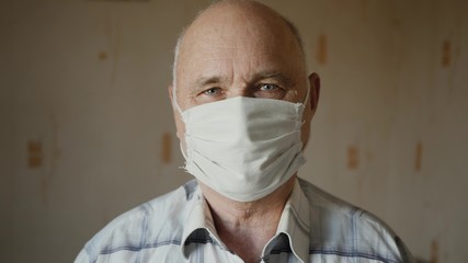 Portrait of an elderly man in handmade homemade protective mask indoors. The concept of health and...