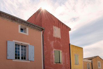 Colorful painted houses in a village in France.  A sun star is at the peak of one roof with sun rays.