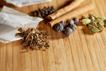 Close up of an open herbal tea bag with loose herbs and juniper berries, cinnamon sticks, allspice, star anise and cardamom on a bamboo cutting board with shallow depth of field