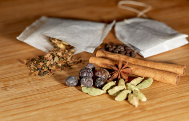 Close up of an open herbal tea bag with loose herbs and juniper berries, cinnamon sticks, allspice, star anise and cardamom on a bamboo cutting board with shallow depth of field