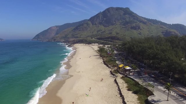 aerial footage of a beach with green mountain, nature and waves in a sunny day at brazil, rio de janeiro, recreio dos bandeirantes, macumba beach. Almost empty, without people. by drone dji phantom