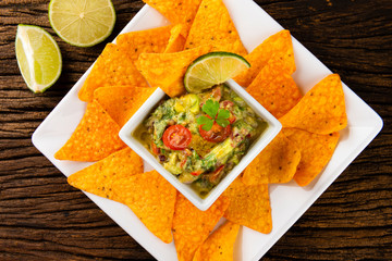Avocado guacamole, lime, tomato, onion and cilantro, served with nachos on an old wooden table. Vegan food.