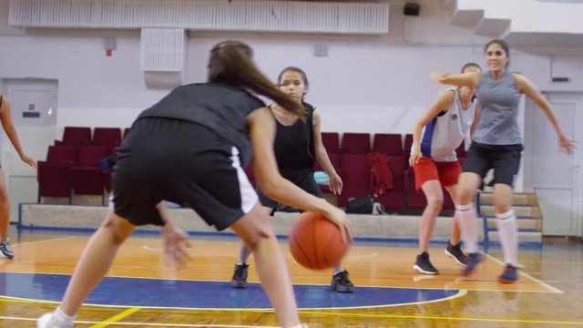 Young multiethnic female athletes in sportswear playing basketball on indoor court
