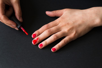 young woman making herself a terrible manicure using red nail polish on black background