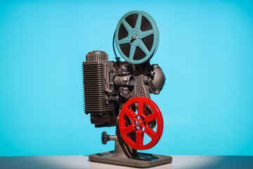 An authentic vintage 8mm film projector. With reels and film, set against a hip modern blue...