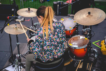 Obraz premium Beautiful young blonde drummer from back with drums and flowery sweatshirt playing live on stage