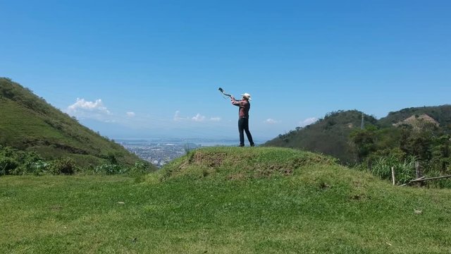 aerial footage in direction of a comboy man playing the Blowing horn to drive the cattle in grass with a panoramic view of a city. Winding horn, gaudy, Drone