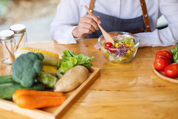 Closeup image of a female chef cooking and eating a bowl of fresh mixed vegetables salad in kitchen